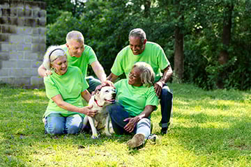 A group of charity volunteers in green shirts seated on the grass, with a dog lying beside them.