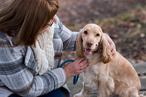 A person in a plaid shirt and white scarf petting a light brown dog with long ears.