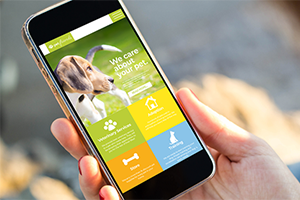 A person holds a smartphone displaying a pet-related app with a beagle on the screen.