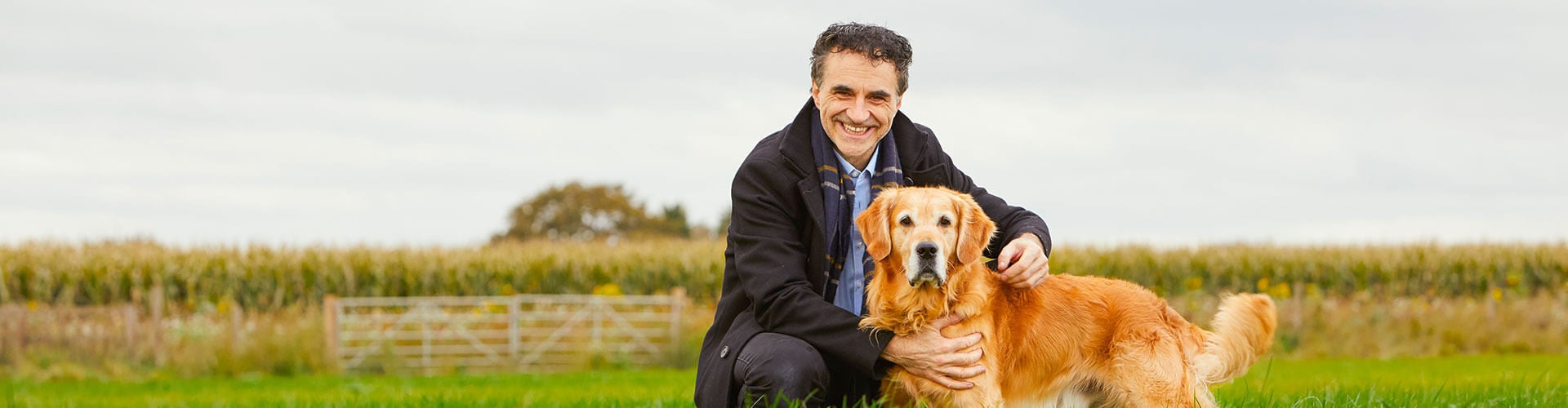 A photo of veterinarian Noel Fitzpatrick next to a golden retriever in a grassy field.