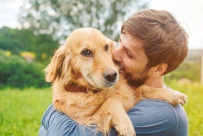 A man with a beard holding a golden retriever, with the dog looking at the camera.
