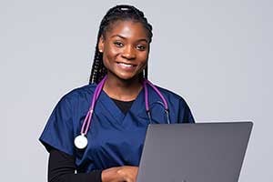 A vet with a stethoscope around their neck typing on a laptop.