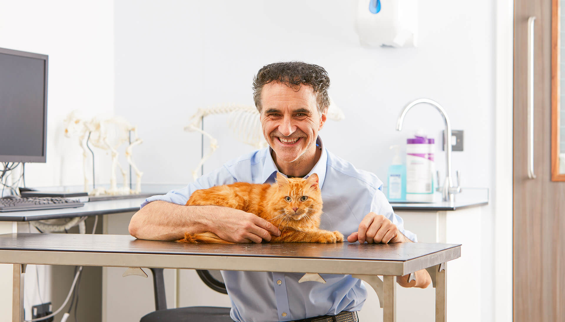 Veterinarian Noel Fitzpatrick holding a ginger cat on an examination table.